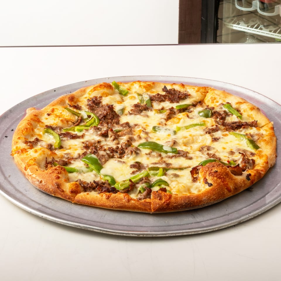 A whole pizza with melted cheese, ground meat, and green peppers on a metal pan.