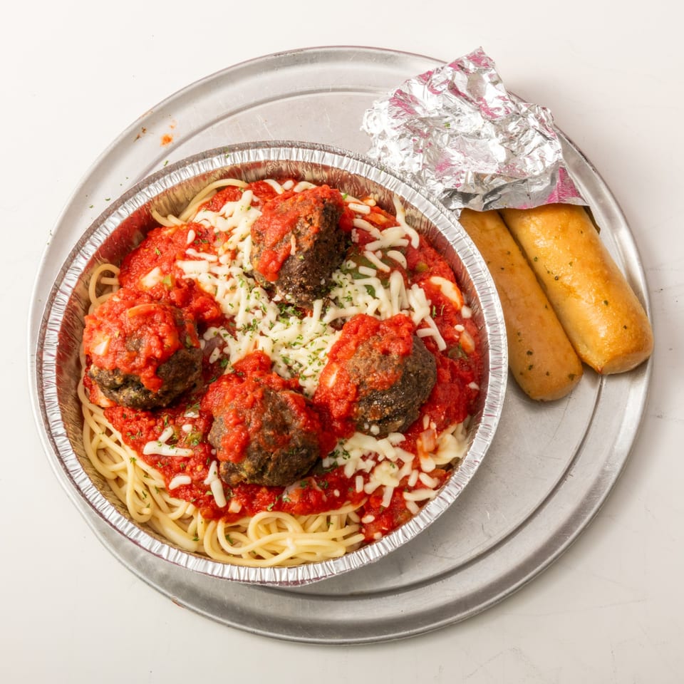 Spaghetti and meatballs with tomato sauce and cheese in a foil container, with two breadsticks.