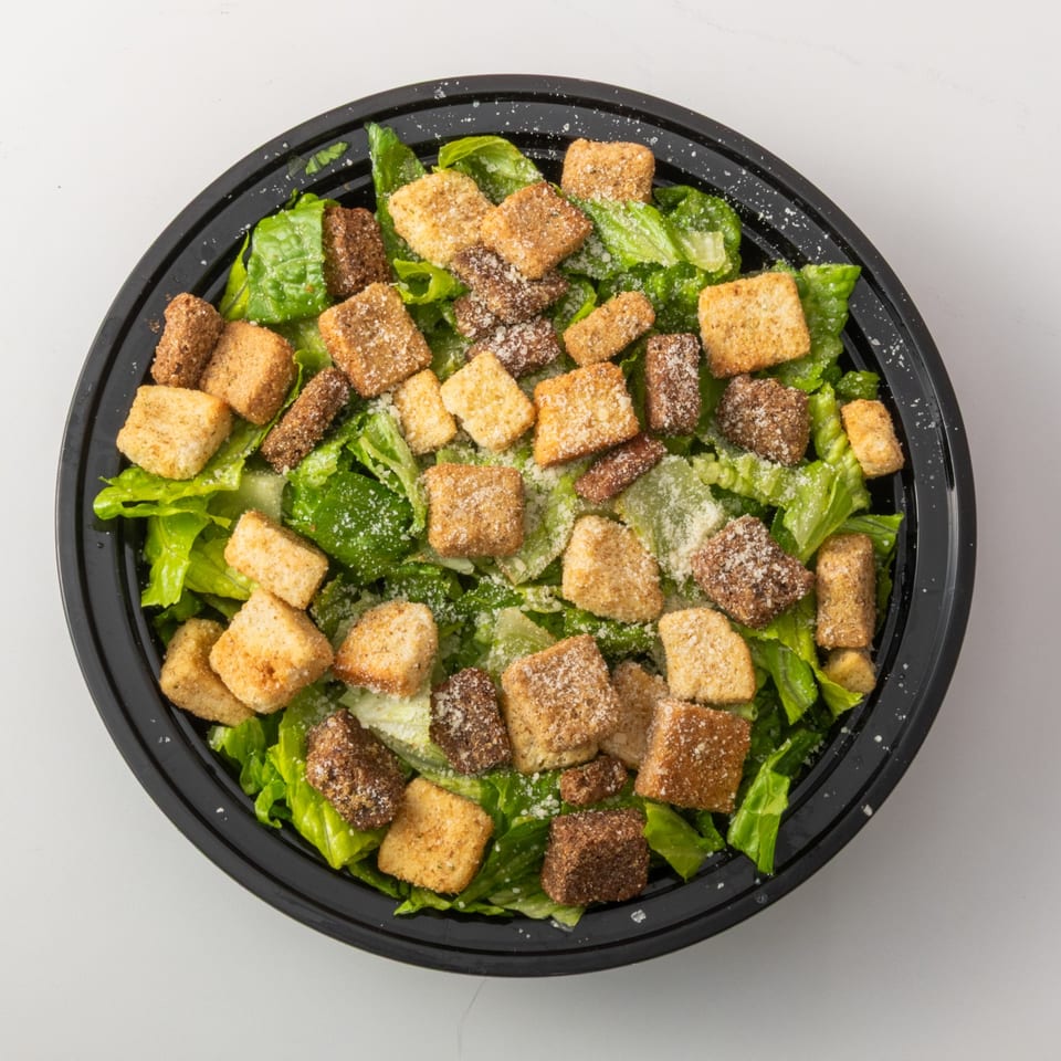 Overhead view of a Caesar salad with romaine lettuce, croutons, and grated cheese in a black bowl.