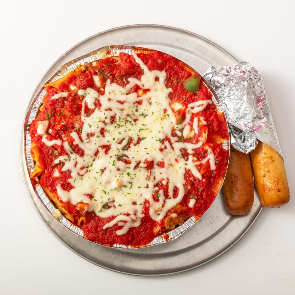 Baked ziti with melted cheese and red sauce, served with two breadsticks on a metal tray.