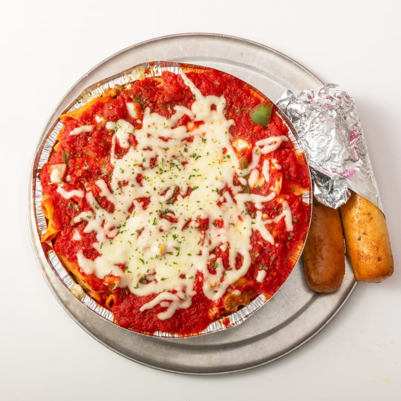 Baked ziti with melted cheese and red sauce, served with two breadsticks on a metal tray.