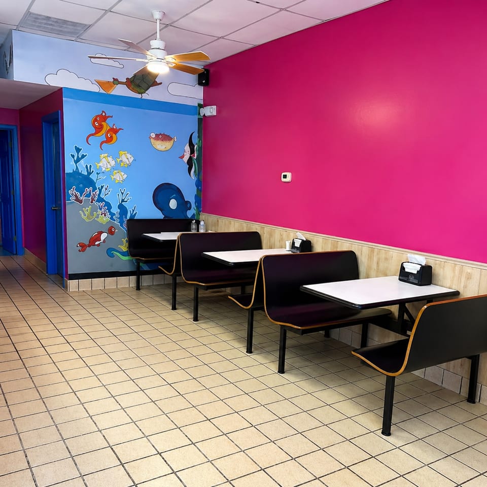 Restaurant interior with bright pink and blue walls, ocean-themed murals, and black booth seating.