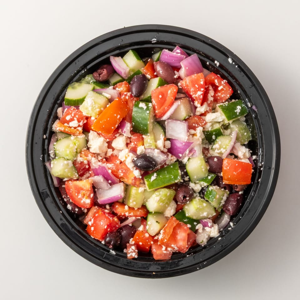 Overhead view of a vibrant Greek salad with tomatoes, cucumbers, red onions, olives, and feta cheese.